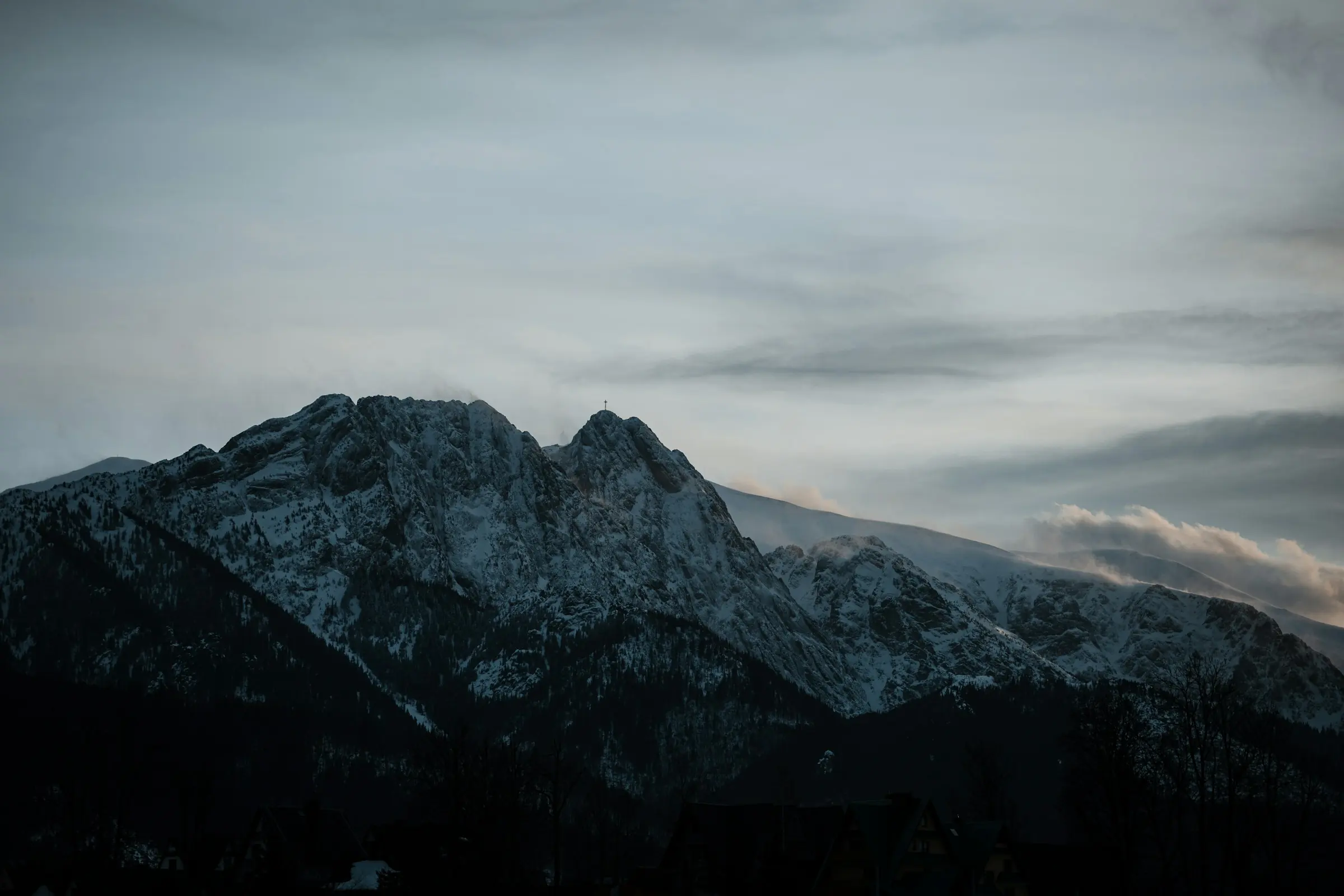 Giewont zimą: ośnieżona grań z krzyżem na tle zachmurzonego nieba