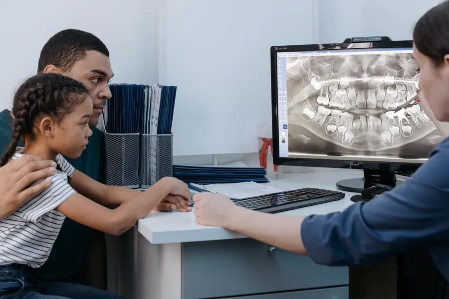 Lekarka omawia zdjęcie pantomograficzne z tatą i córką przy monitorze