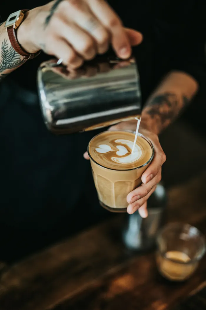 Barista wlewa spienione mleko do szklanki, na powierzchni powstaje wzór