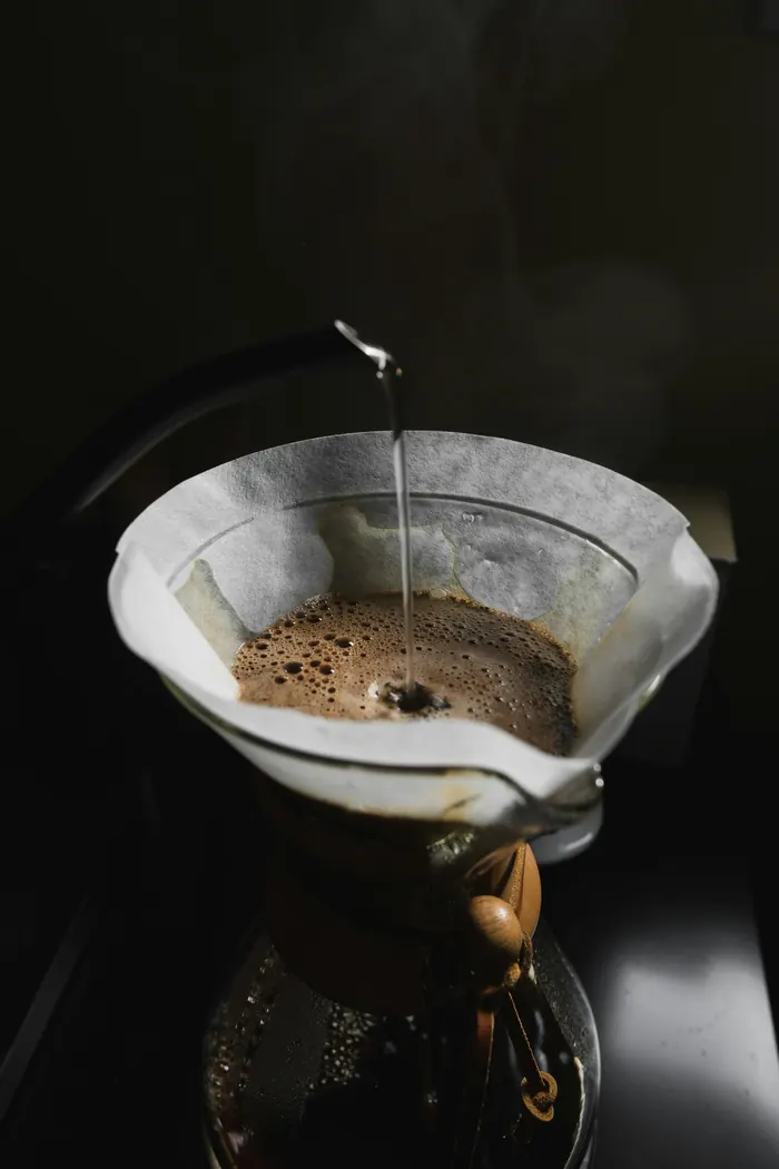 Woda z czajnika spływa cienkim strumieniem na kawę w filtrze Chemexa